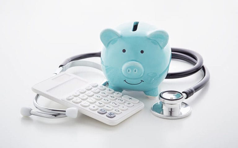 Three objects: A calculator, stethoscope, and blue money pig.
