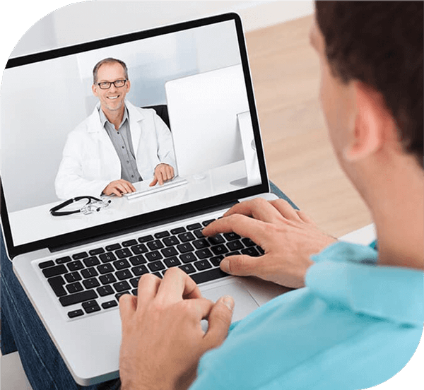 A patient sitting with a laptop speaking with a doctor in a video conference.