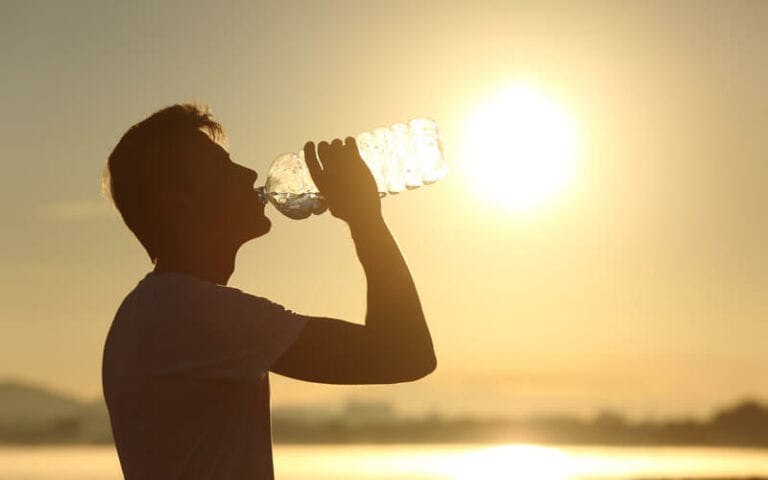 A silhouette of a man drinking from a water bottle. The setting sun is in the background.