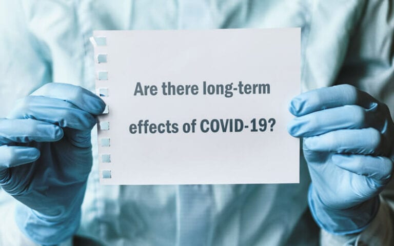 A doctor holding a piece of paper that reads "Are there long-term effects of COVID-19?"