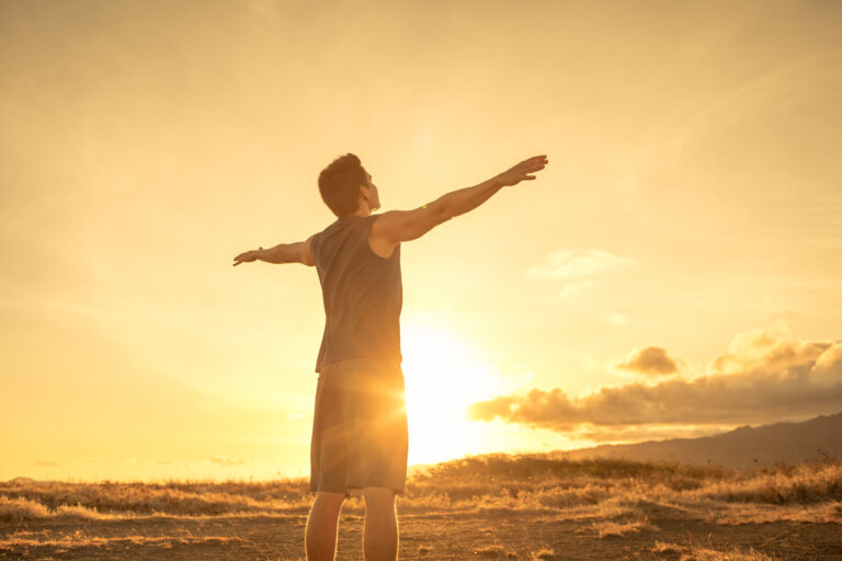 A man standing outside with arms outstretched while the sun slowly goes down.