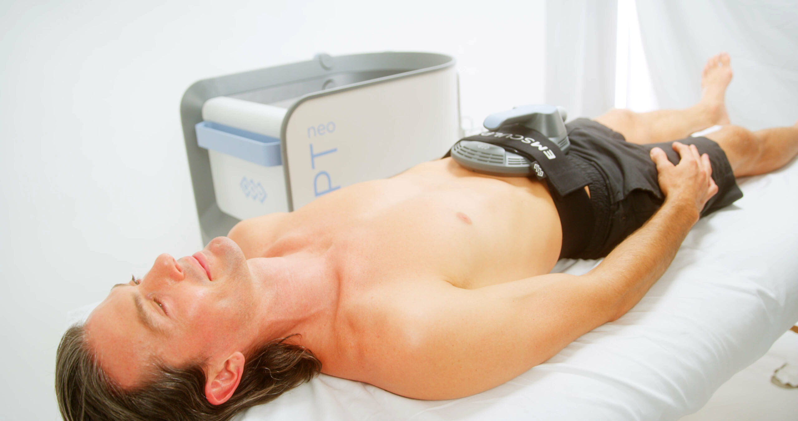 A man laying on a bed using the EMSCULPT NEO treatment